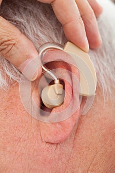 Doctor inserting hearing aid in senior man's ear