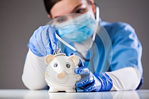 Doctor inspecting piggy bank with stethoscope