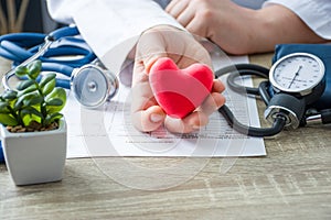 Doctor of internal medicine and cardiologist holding in his hands and shows to patient figure of red card heart during medical con photo