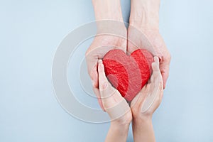 Doctor and kid holding red heart in hands top view. Family relationships, health care, pediatric cardiology concept. photo