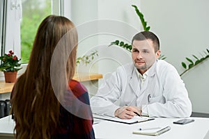 A doctor in lab coat is listening to a female patient`s complaints in a hospital