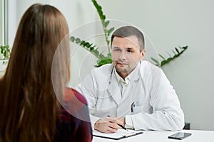 A doctor in lab coat is listening to a female patient`s complaints in a hospital