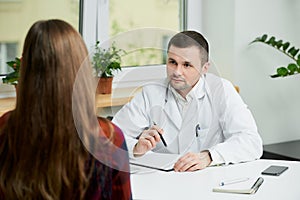 A doctor in lab coat is listening to a female patient`s complaints in a hospital