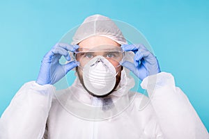 Doctor or lab scientist wearing biohazard protective suit puts on safety glasses, close-up of face. Coronavirus, covid