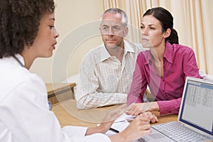 Doctor with laptop and couple in doctor's office