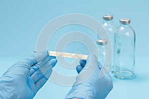 Doctor in latex gloves holding a glass mercury thermometer on blue background