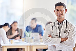 A doctor that likes to make a difference. a young male doctor standing with his arms crossed in an office at work.