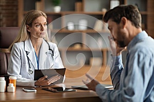 Doctor listening male patient telling about health problems during meeting in office