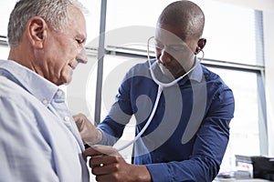 Doctor Listening To Chest Of Senior Male Patient During Medical Exam In Office