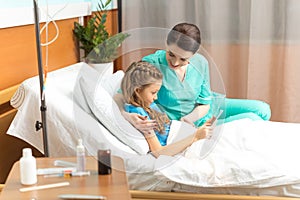 Doctor and little girl using digital tablet and sitting on bed