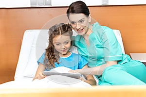 Doctor and little girl using digital tablet and sitting on bed