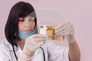 Doctor looking at fifty euro banknote holding it in gloves