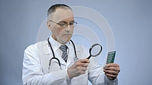 Doctor looking at pack of pills through magnifying glass, counterfeit medication