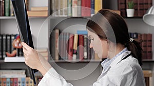 Doctor looks at X-RAY or MRI scan. Concentrated woman doctor in white coat at workplace in office reads MRI or X-ray