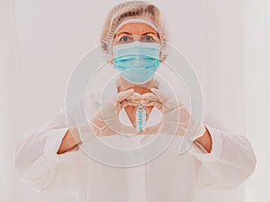 Doctor with mask makes a heart with her hands and covid-19 vaccine photo