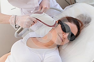 The doctor makes laser hair removal on the face of a woman in the salon. An alternative way to permanently remove