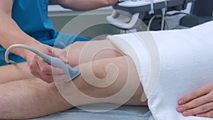 Doctor makes ultrasound of knee joint for man using ultrasound scanner, closeup.