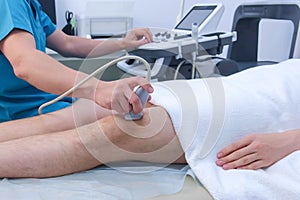 Doctor makes ultrasound of knee joint for man using ultrasound scanner, closeup.