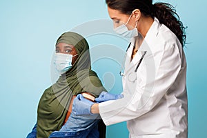 Doctor Making Vaccine Injection To African Muslim Lady, Blue Background