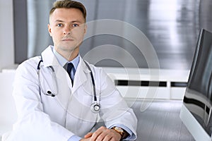 Doctor man sitting behind a computer at workplace in clinic or hospital office. Medic headshot and medicine concept