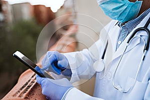 doctor man taking a break, using mobile phone. Wearing protective gloves, mask and stethoscope. coronavirus covid-19 concept