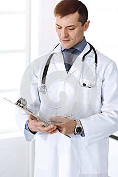 Doctor man using clipboard for filling up medication history record. Perfect medical service. Physician at work in