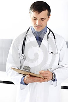 Doctor man using clipboard for filling up medication history records. Perfect medical service in clinic. Physician at