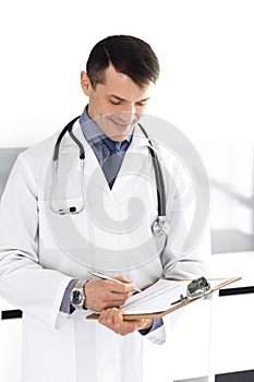 Doctor man using clipboard for filling up medication history records. Perfect medical service in clinic. Physician at