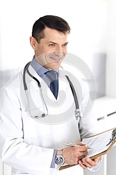 Doctor man using clipboard for filling up medication history records. Perfect medical service in clinic. Physician at