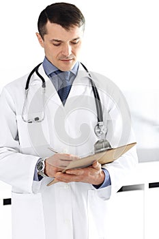 Doctor man using clipboard for filling up medication history records. Perfect medical service in clinic. Physician at