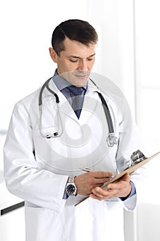 Doctor man using clipboard for filling up medication history records. Perfect medical service in clinic. Physician at