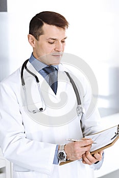 Doctor man using clipboard for filling up medication history records. Perfect medical service in clinic. Physician at