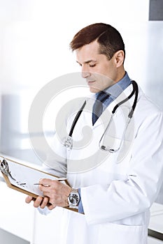Doctor man using clipboard for filling up medication history records. Perfect medical service in clinic. Physician at