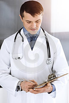 Doctor man using clipboard for filling up medication history records. Perfect medical service in clinic. Physician at