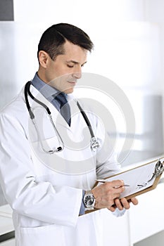 Doctor man using clipboard for filling up medication history records. Perfect medical service in clinic. Physician at