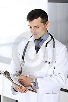 Doctor man using clipboard for filling up medication history records. Perfect medical service in clinic. Physician at