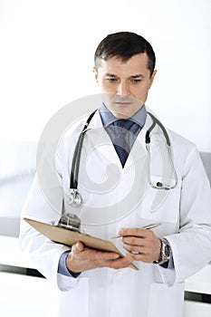 Doctor man using clipboard for filling up medication history records. Perfect medical service in clinic. Physician at