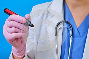 Doctor with a marker in hand, close-up. A nurse in a medical uniform writes with a pen, blue background