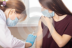 Doctor in mask giving an injection of a vaccine to a teenager girl in a medical clinic, vaccine prevention against infection with