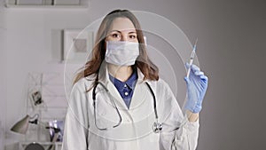 A doctor in a mask and gloves holds a syringe filled with liquid