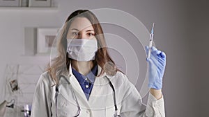 A doctor in a mask and gloves holds a syringe and sprays liquid out of it