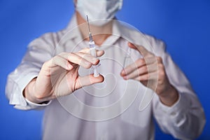 Doctor in mask with a injection syringe on the blue background