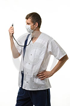 Doctor in a mask looks at a phonendoscope dressed on himself