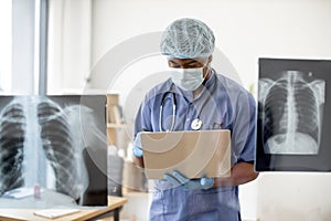 Doctor in mask and scrubs examining X-ray scans via laptop