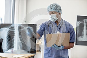 Doctor in mask and scrubs examining X-ray scans via laptop