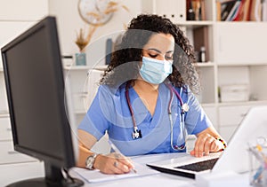 Doctor in mask working on laptop