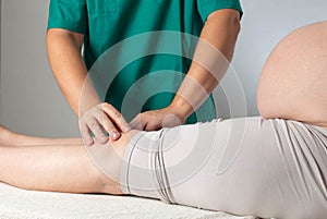 Doctor massage therapist makes massage on the legs and knee joints of a pregnant girl. Childbirth