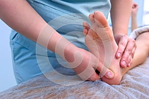 Doctor massagist making therapy massage to child boy on foot in clinic, closeup.