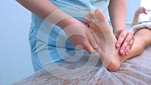 Doctor massagist making therapy massage to child boy on foot in clinic, closeup.