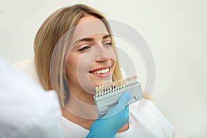 Doctor matching patient`s teeth color with palette on light background. Cosmetic dentistry